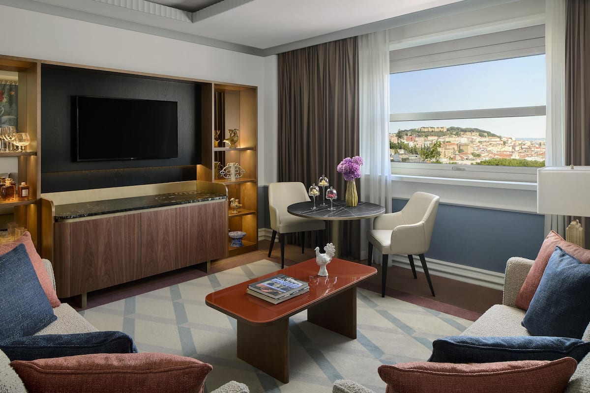 Ein modernes Hotelzimmer mit Fernseher, Sitzecke, Esstisch und Blick auf eine Stadtlandschaft.