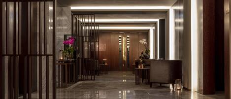 A modern hotel lobby with a marble floor, wooden reception desk, and a large mirror.