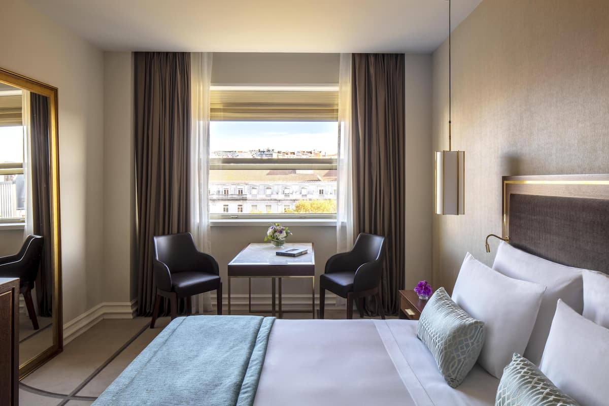 Ein Hotelzimmer mit einem Bett, zwei Stühlen, einem kleinen Tisch mit einer Vase und einem Fenster mit Vorhängen.