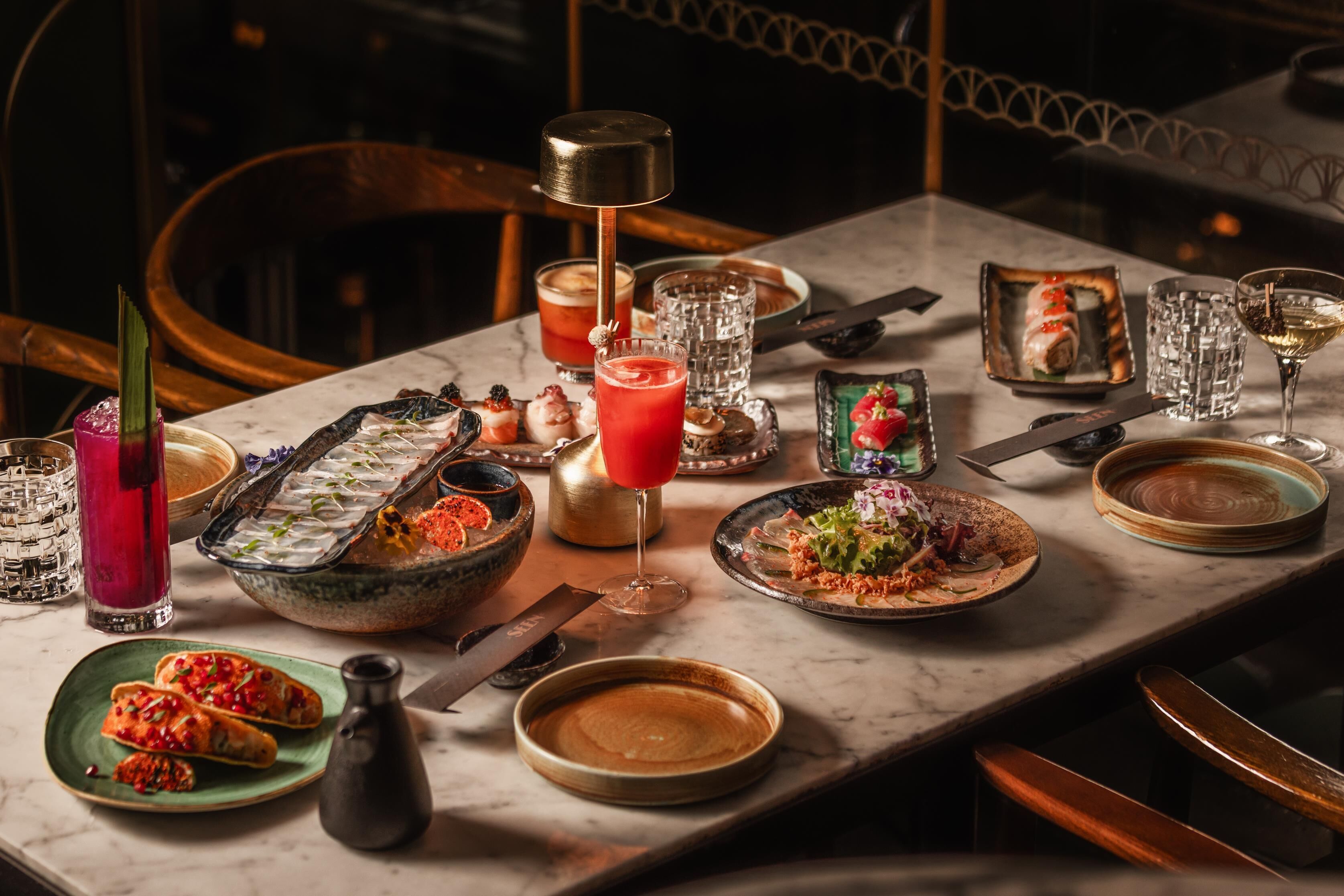 Una mesa de comedor con diferentes platos, vasos y un cóctel.
