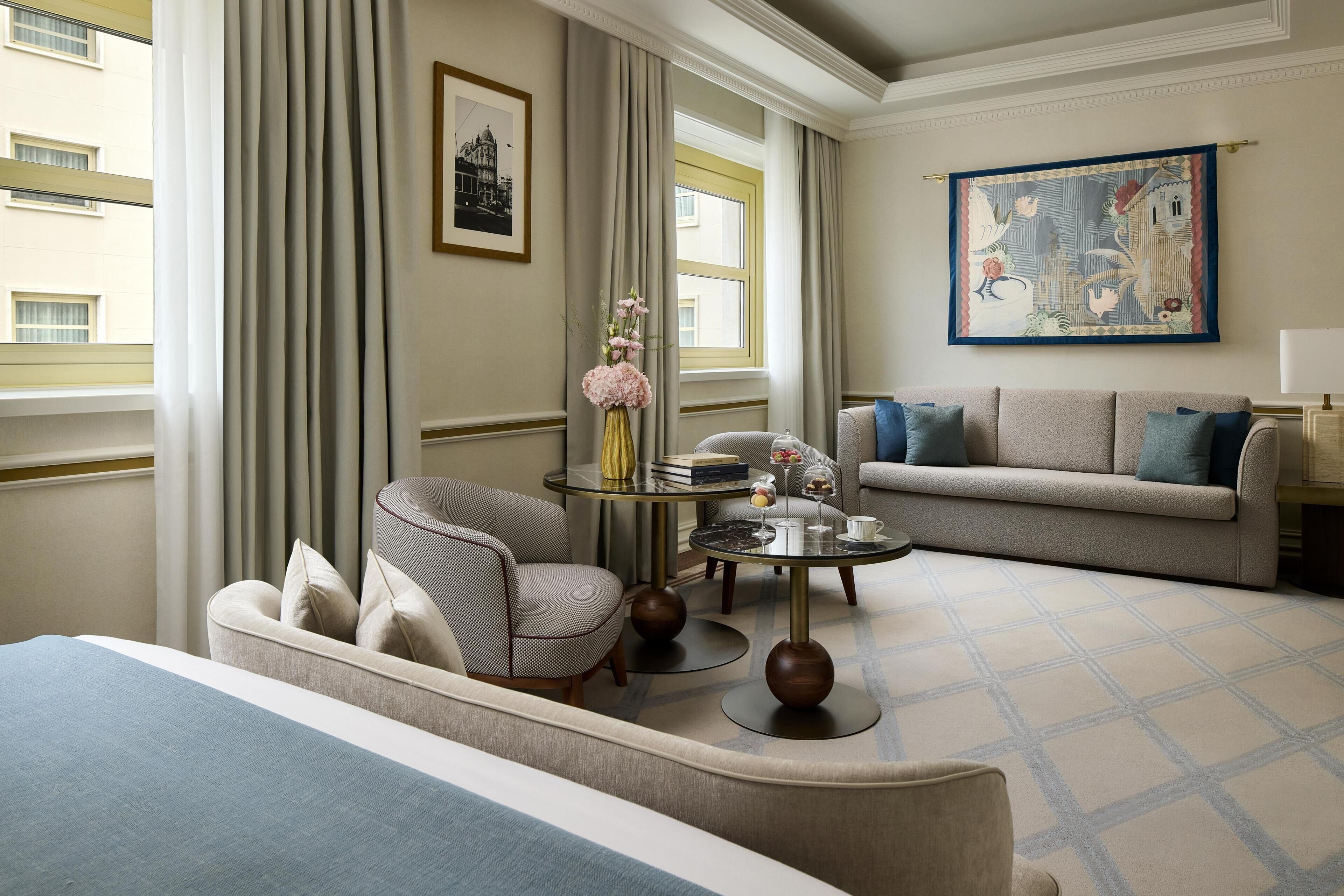 Habitación de hotel con cama, sofá, sillón, una mesita redonda con un florero y un cuadro en la pared.
