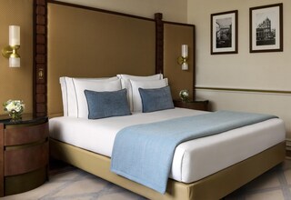 A hotel room with a large bed, two bedside tables, a nightstand, a wall-mounted lamp, and two framed pictures.