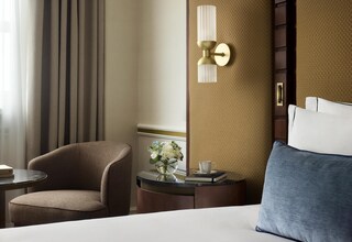 A hotel room with a bed, a chair, a small table with a vase of flowers, a cup, and a book.