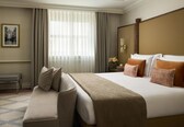 A hotel room with a large bed, a bench, a nightstand with a lamp, and a framed picture on the wall.