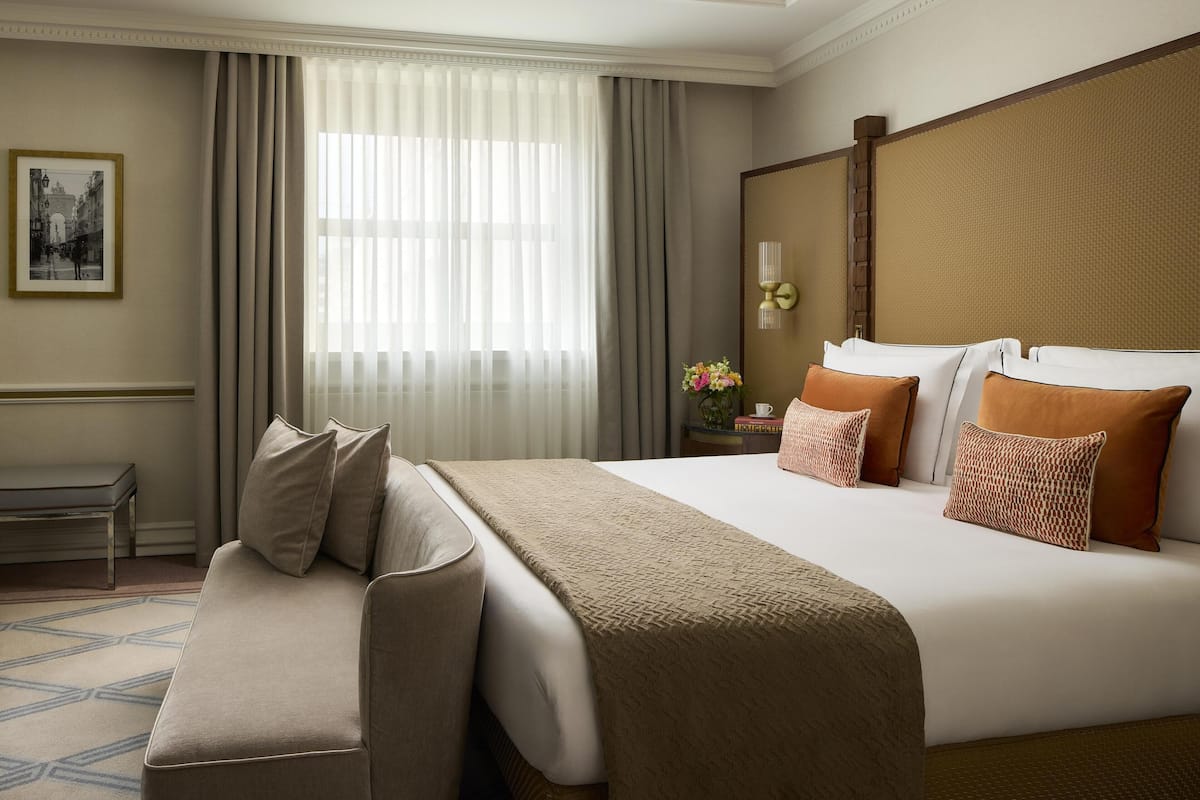 Ein Hotelzimmer mit einem großen Bett, einer Sitzbank, einem Nachttisch mit Lampe und einem gerahmten Bild an der Wand.