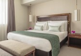 A hotel room with a large bed, a bench, a nightstand, and a wall-mounted lamp.