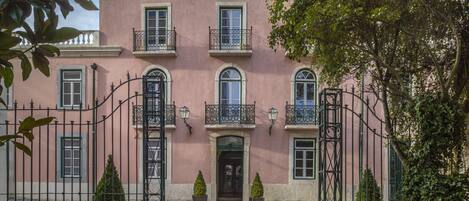 A pink building with a central entrance, two potted plants, and a cobblestone courtyard.