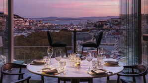 Mesa de comedor para dos personas con vista a la ciudad, dos sillas y varios vasos.