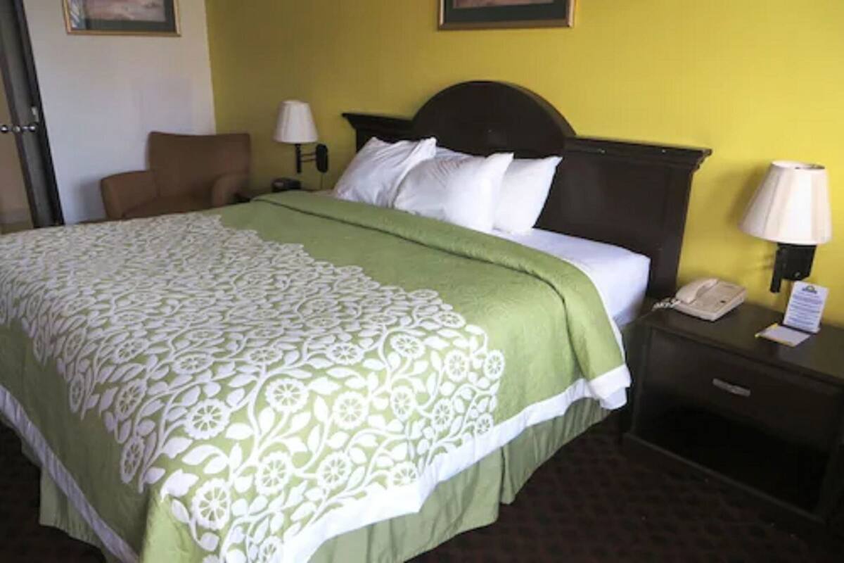 A hotel room with a bed, a nightstand with a lamp, a chair, and a door.