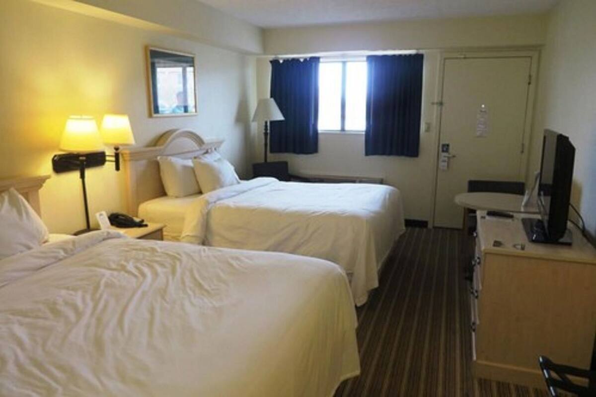 A hotel room with two beds, a desk with a computer, a lamp, and a window with curtains.