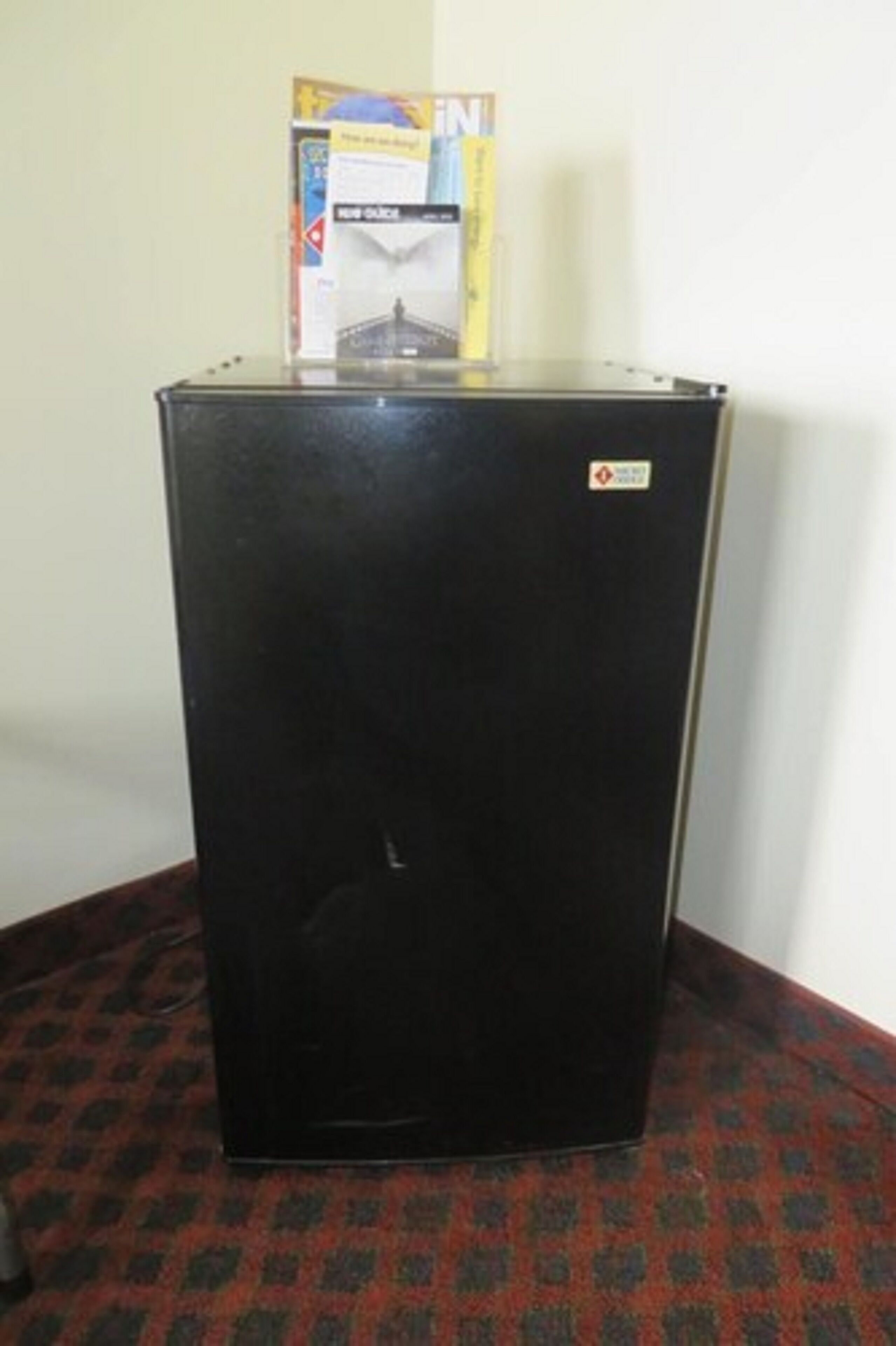 Un refrigerador negro con un adhesivo en la puerta, sobre una alfombra estampada.