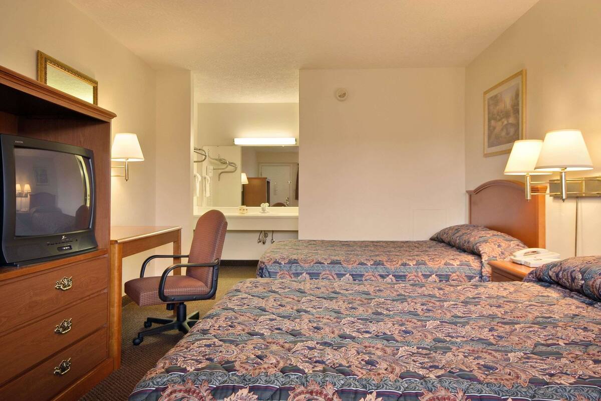 A hotel room with a bed, a desk with a television, a chair, a bathroom with a mirror, and two bedside lamps.