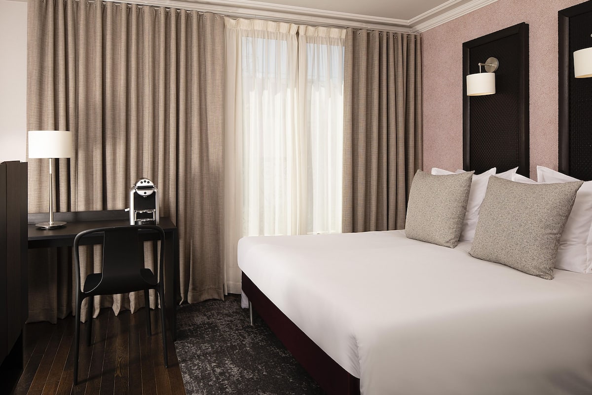 A hotel room with a bed, a desk, a chair, and a lamp.
