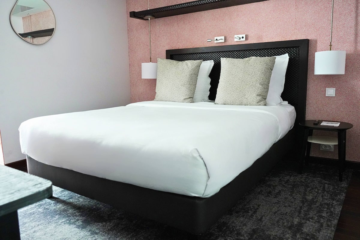 A neatly made bed with white linens, a dark headboard, and two bedside lamps.