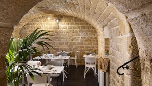 Un comedor con paredes de piedra, mesas y sillas, una planta en maceta y una lámpara colgante.
