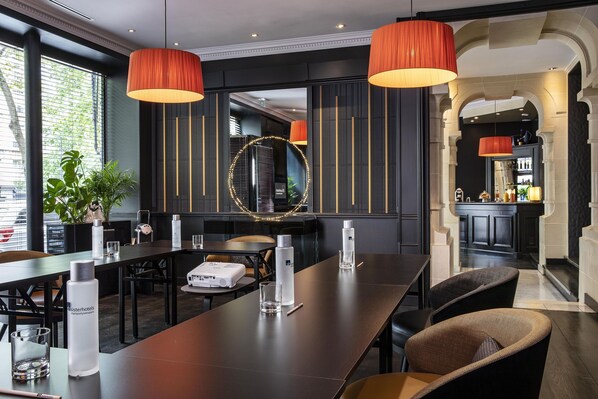 A modern hotel lobby with a long reception table, dark wood flooring, and large orange pendant lights.