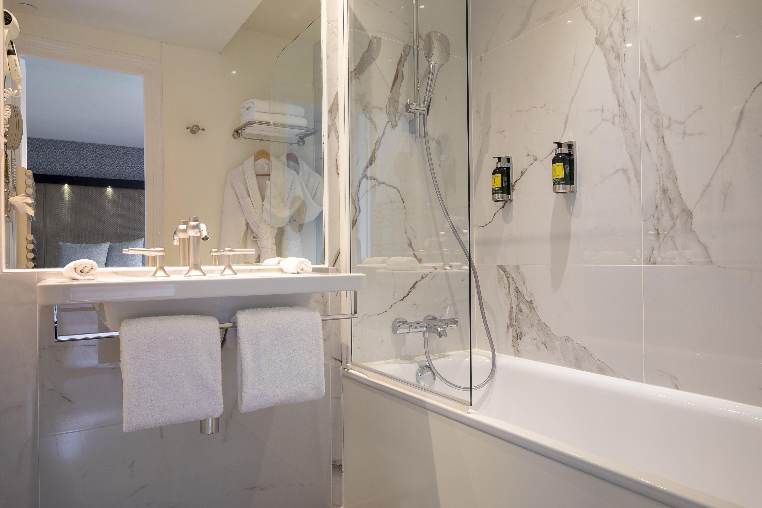 A modern bathroom with a glass-enclosed shower, a white bathtub, and a vanity with a mirror and towel rack.