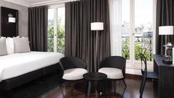 A hotel room with a bed, two chairs, a small table, and a desk with a lamp.