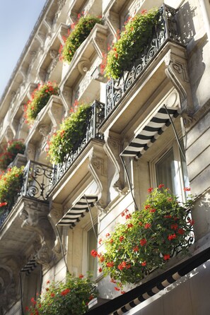 A building facade with multiple balconies adorned with red flowers and black wrought iron railings.