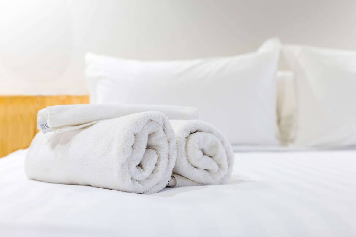A neatly made bed with white linens and rolled towels.