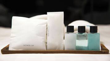 A wooden tray with a white shower cap, a white cotton bud, a conditioner bottle, a shower gel bottle, and a shampoo bottle.