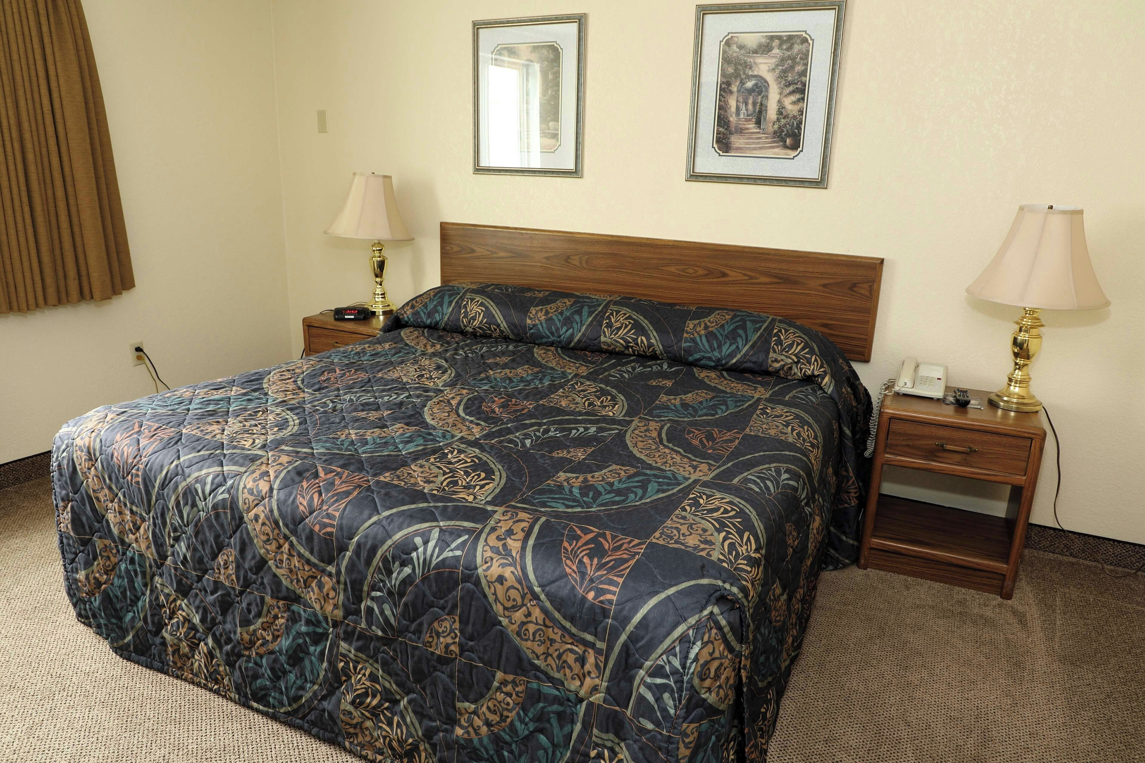 Habitación de hotel con cama, dos mesitas de noche, lámpara y dos cuadros en la pared.