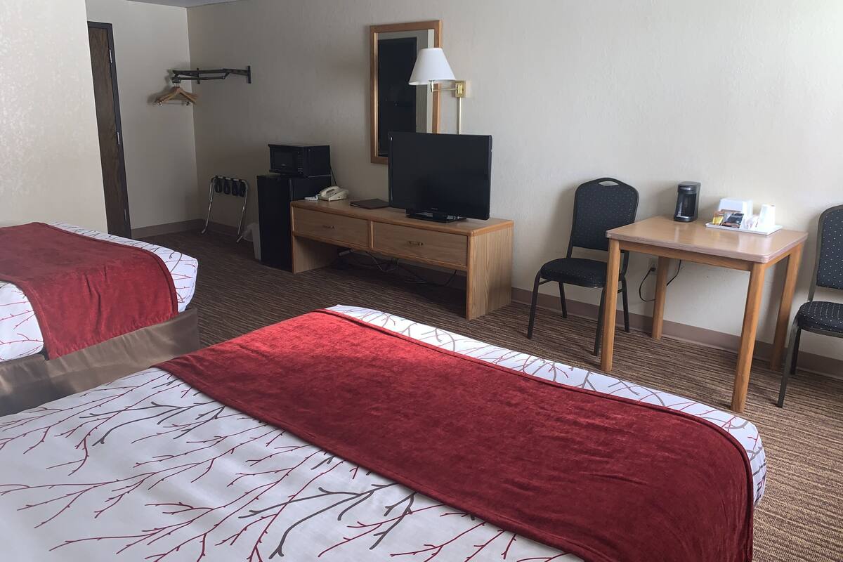 A hotel room with two beds, a desk, a chair, a television, a lamp, and a coffee maker.
