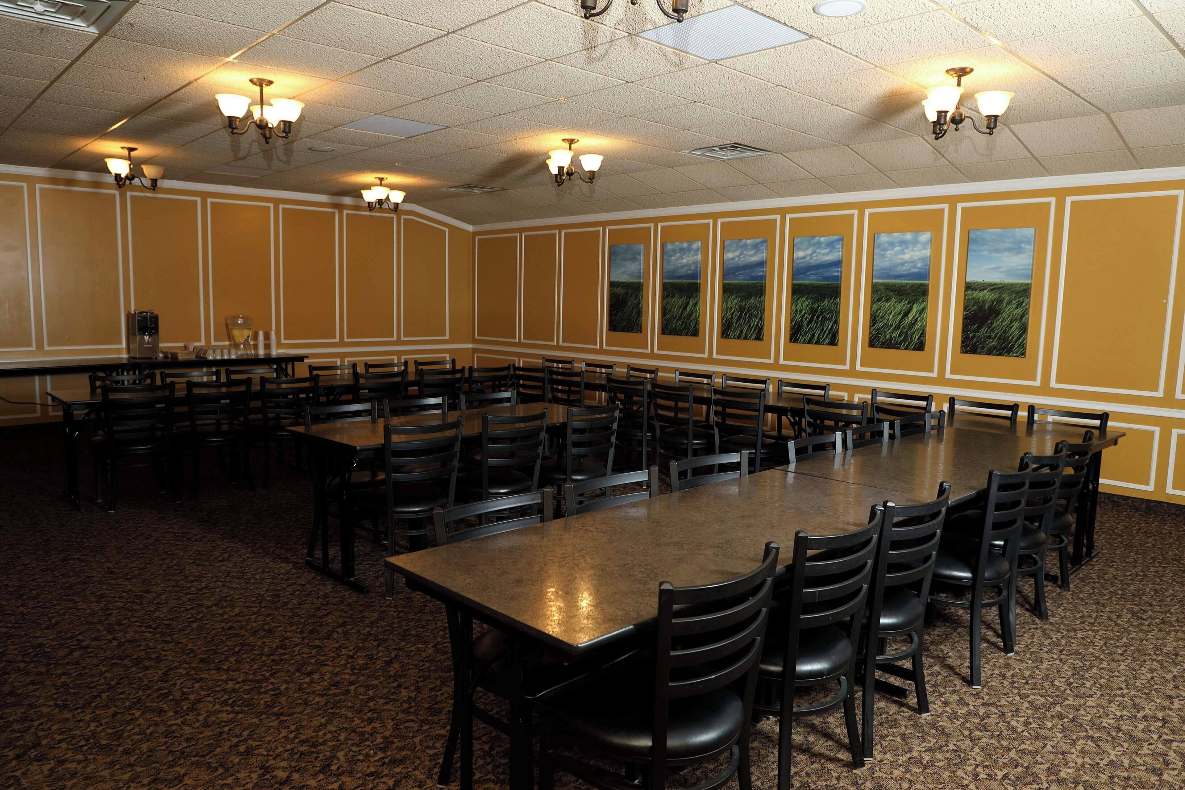 Une salle de conférence dotée de plusieurs tables et chaises, d’un éclairage au plafond et de grandes fenêtres offrant une vue sur le paysage.