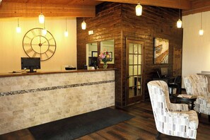 A reception area with a wooden wall, a large clock, a reception desk, and two patterned armchairs.