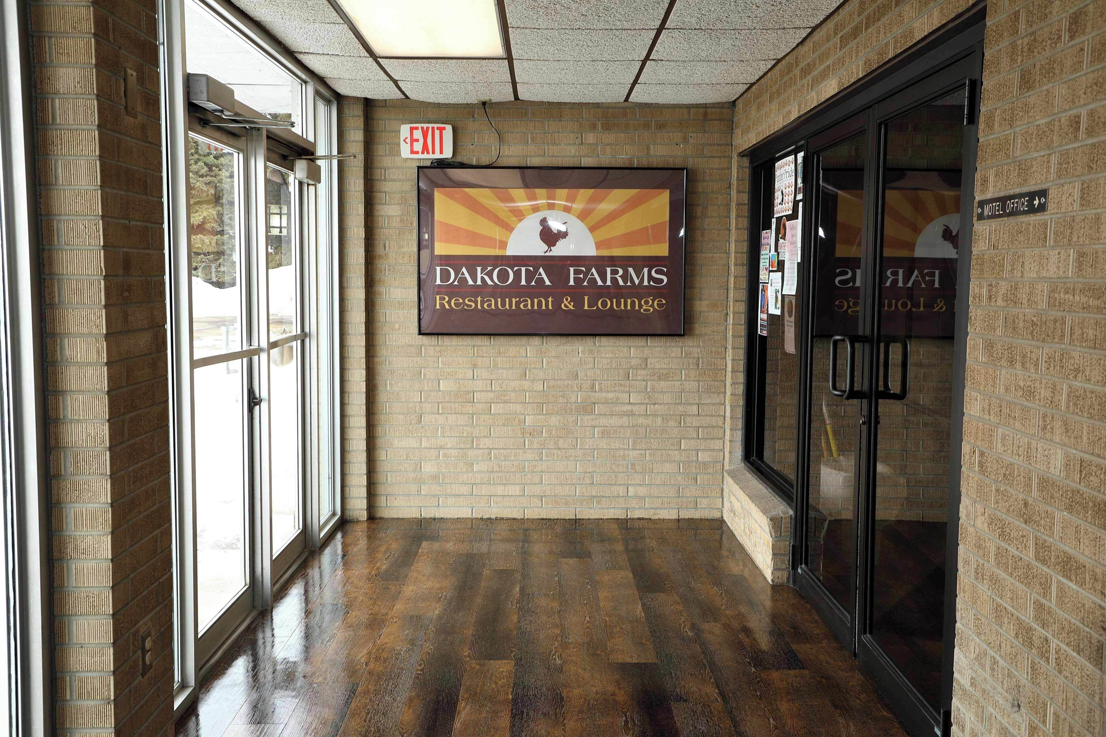 Un pasillo con un cartel de Dakota Farms Restaurant & Lounge, un letrero de salida y una puerta de vidrio que da a la recepción.