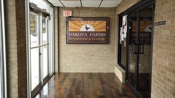 Un pasillo con un cartel de Dakota Farms Restaurant & Lounge, un letrero de salida y una puerta de vidrio que da a la recepción.