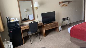 A hotel room with a wooden desk, a television, a chair, a microwave, a heater, and a bed with a red cover.