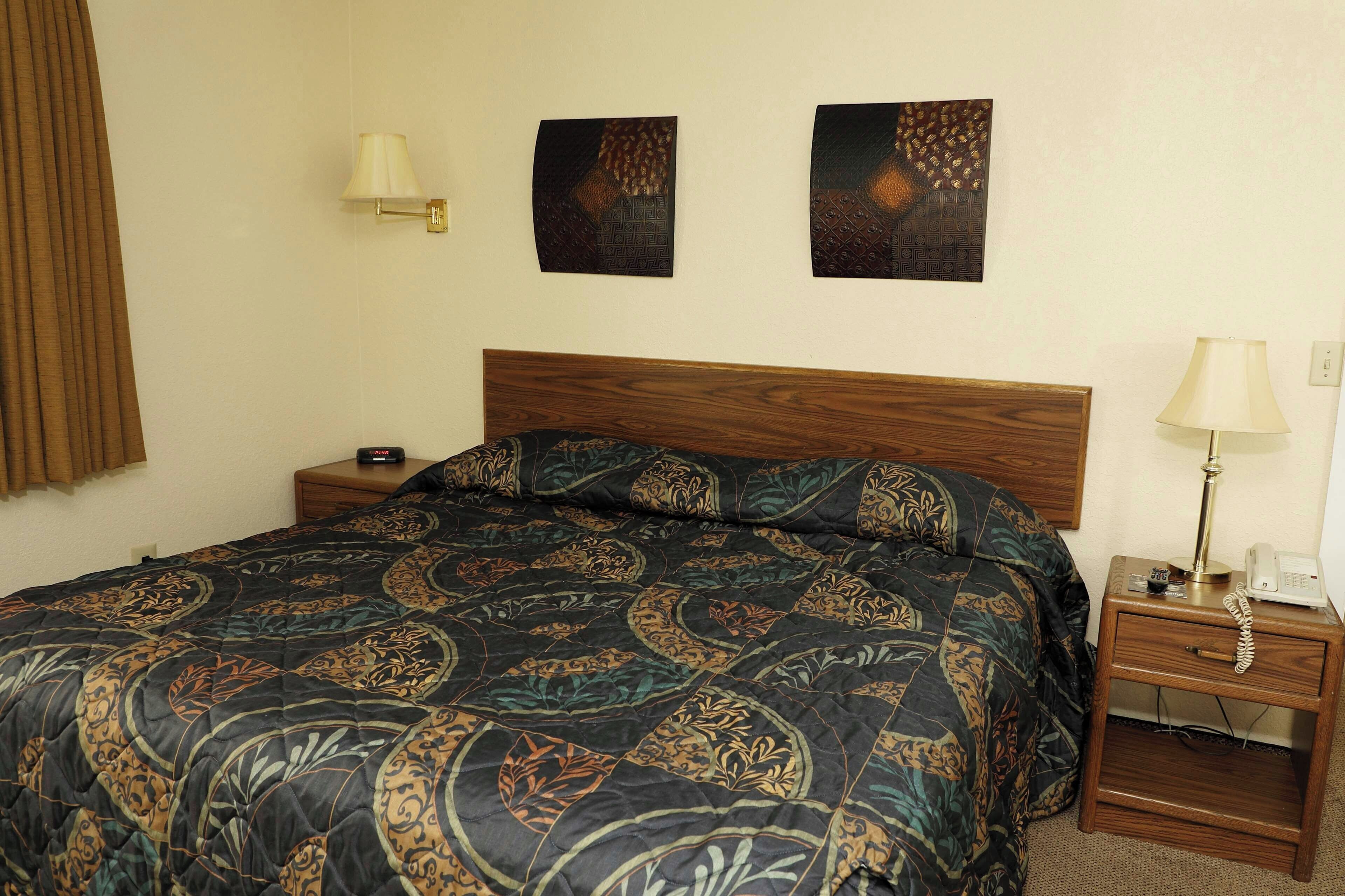 Una habitación de hotel con una cama, una mesita de noche con lámpara y dos obras de arte colgadas en la pared.