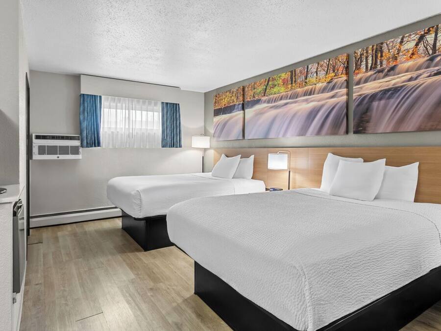 A hotel room with two beds, a flat-screen TV, air conditioning, a painting of a waterfall, and a window with curtains.