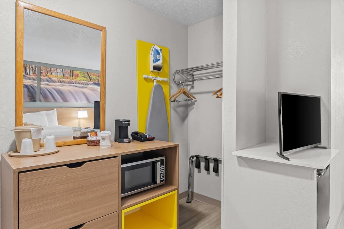 A hotel room with a wooden desk, a microwave, a coffee maker, a telephone, a television, and a mirror.