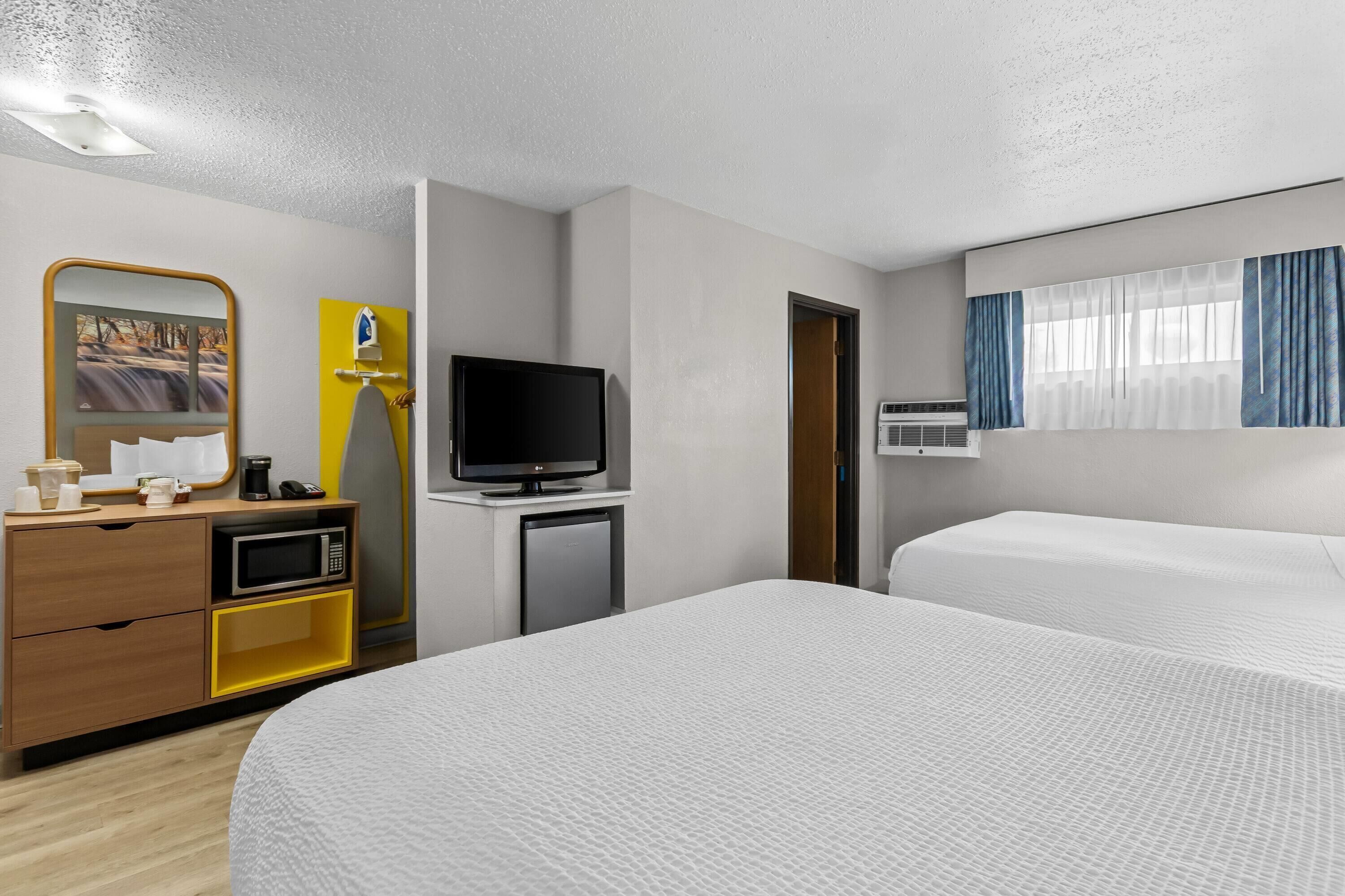 A hotel room with a bed, a TV, a desk with a microwave, and a mirror.