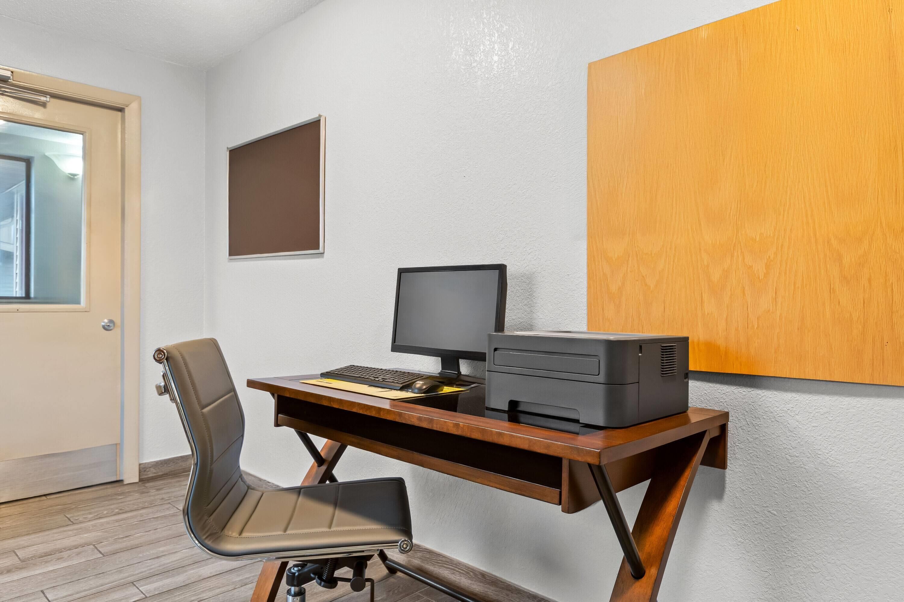 A room with a wooden desk, a chair, a computer monitor, and a printer.