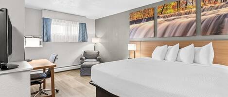 A hotel room with a bed, desk, chair, and wall-mounted artwork.
