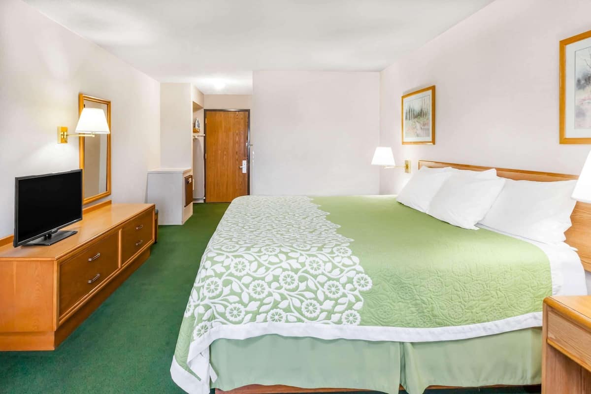 A hotel room with a bed, a television on a wooden dresser, a door, and a wall-mounted lamp.