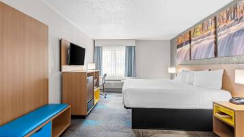 Habitación de hotel con cama, escritorio, televisión, ventana con cortinas y un cuadro en la pared.