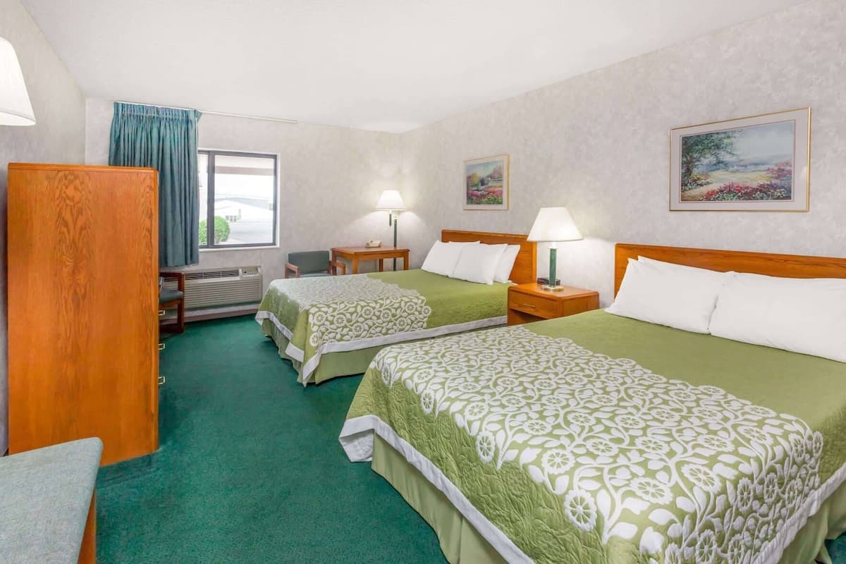 A hotel room with two beds, a desk, a chair, a window with curtains, and a painting on the wall.
