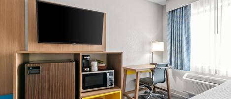 A hotel room with a flat-screen TV, a microwave, a mini-fridge, a desk with a chair, and a bed.