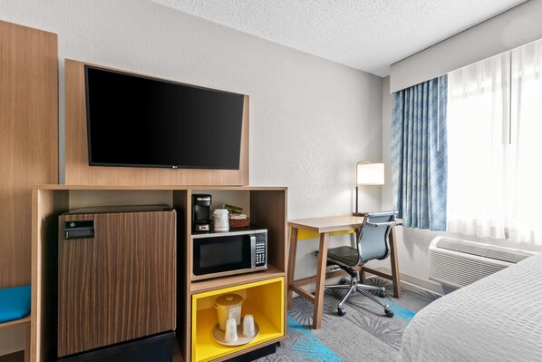 A hotel room with a flat-screen TV, a microwave, a mini-fridge, a desk with a chair, and a bed.