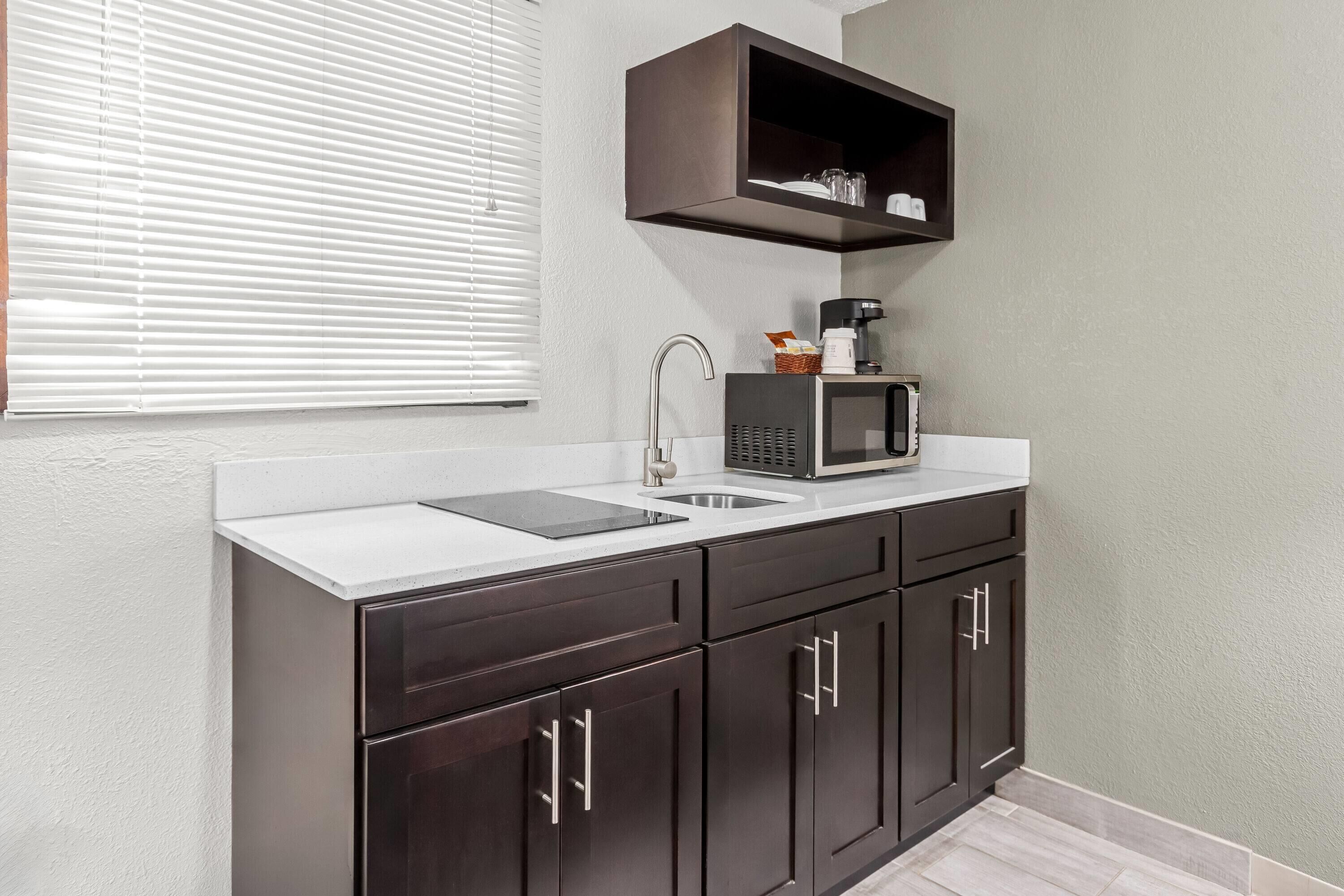 A kitchen with dark cabinets, a white countertop, a microwave, and a coffee maker.