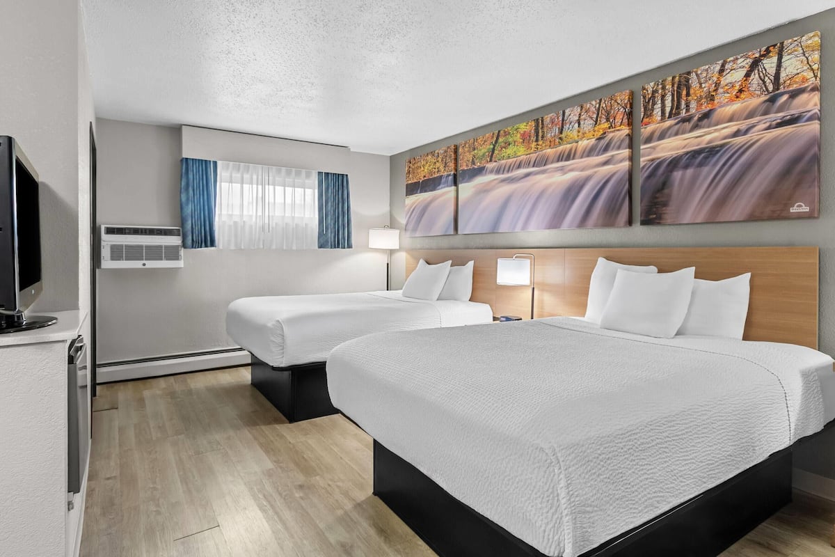 A hotel room with two beds, a TV, air conditioning, a painting of a waterfall, and a window with curtains.