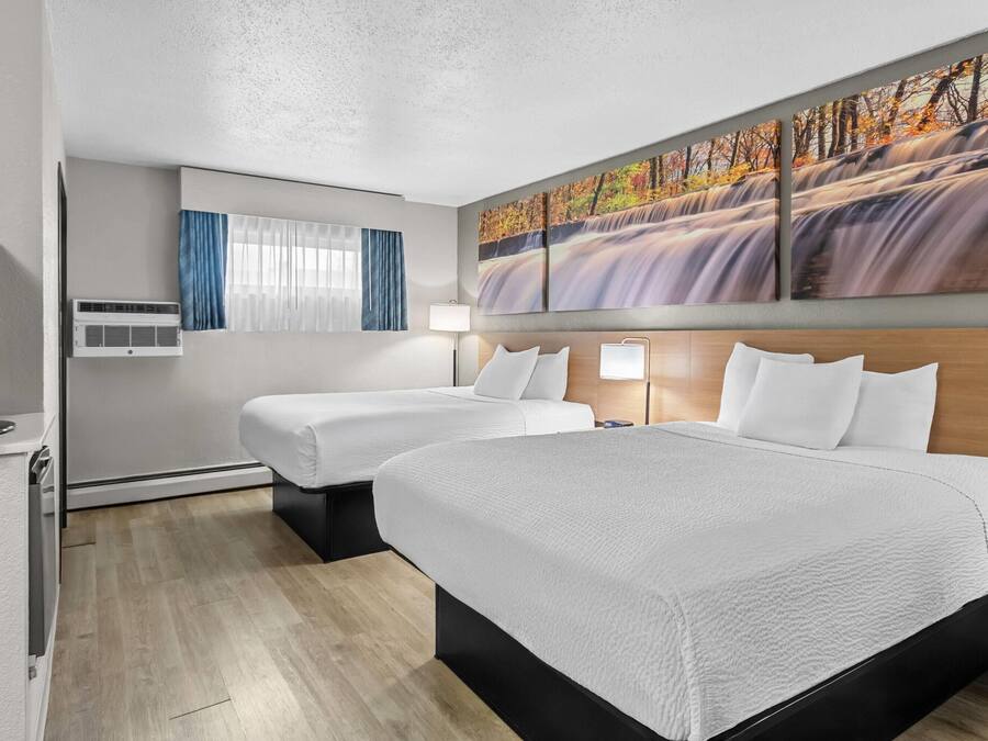 A hotel room with two beds, a TV, air conditioning, a painting of a waterfall, and a window with curtains.