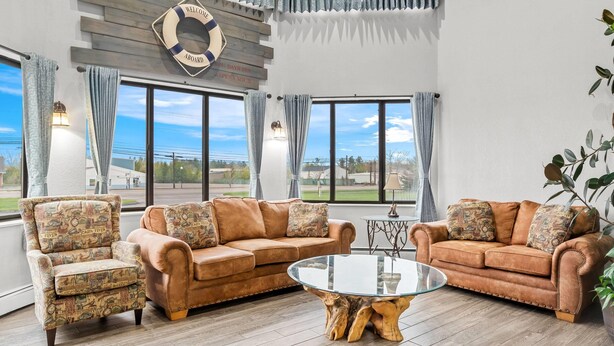 A spacious living area with two brown sofas, a glass coffee table, and a wooden accent piece. - Days Inn by Wyndham Alpena (Alpena)