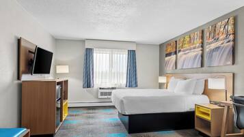 A hotel room with a bed, a desk, a TV, a window with curtains, and artwork on the wall.