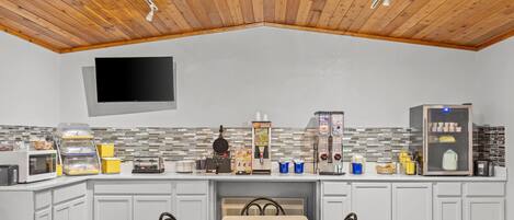 A modern kitchen with white cabinets, a wooden ceiling, a flat-screen TV, and various appliances.