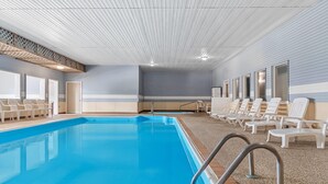 A swimming pool with lounge chairs, a ceiling with linear patterns, and a door. - Days Inn by Wyndham Alpena (Alpena)